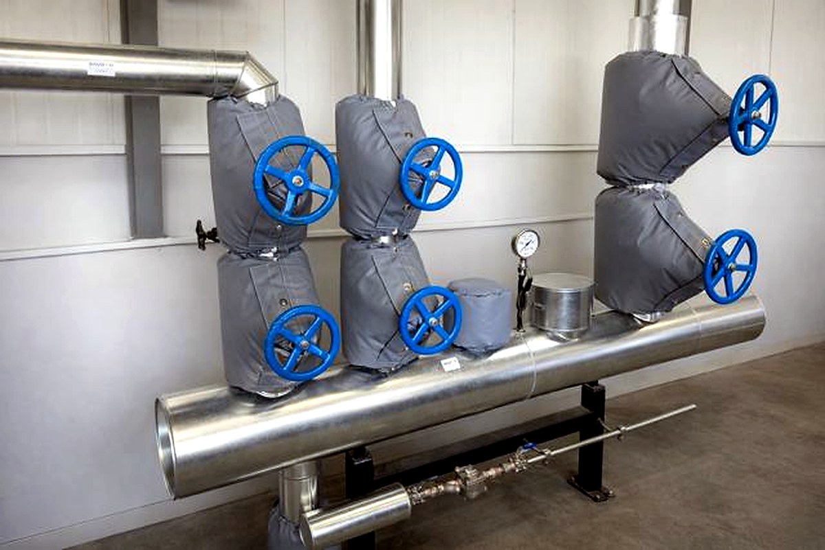 Row of grey thermal jackets on valve assemblies with blue handwheels on a main pipe run